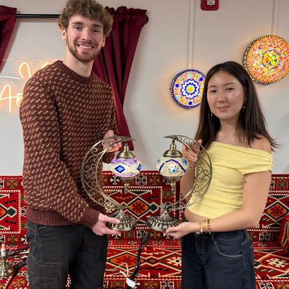 Mosaic Lamp Workshop Two people holding decorative lamps against a colorful wall with patterns.